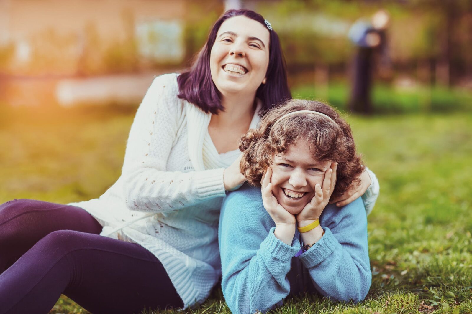 Two people with cerebral palsy lying on the grass looking at the camera and laughing.